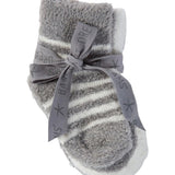 Gray and white striped infant Barefoot Dreams socks with a bow on a beige background. Available at Be Charmed