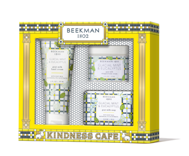 Beekman 1802 Kindness Cafe gift set containing four skincare items: goat milk hand cream, glacial mint & eucalyptus hand cream, glacial mint & eucalyptus jar, and goat milk soap, all in a yellow and blue patterned gift box. Available at Be Charmed