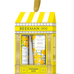 BeeMan 1802 'Kindness Cafe' gift set containing three hand and body care products: a hand cream, a hand wash, and a lip balm, presented in a yellow and white storefront box with a gold hanging loop. Available at Be Charmed
