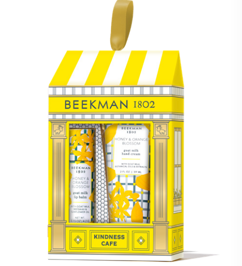 BeeMan 1802 'Kindness Cafe' gift set containing three hand and body care products: a hand cream, a hand wash, and a lip balm, presented in a yellow and white storefront box with a gold hanging loop. Available at Be Charmed
