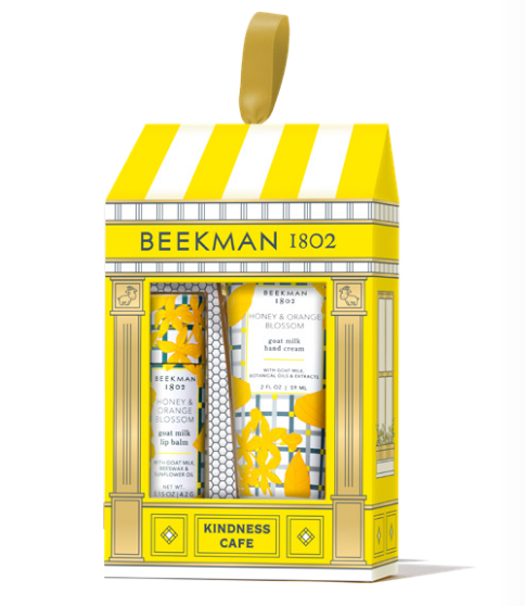 BeeMan 1802 'Kindness Cafe' gift set containing three hand and body care products: a hand cream, a hand wash, and a lip balm, presented in a yellow and white storefront box with a gold hanging loop. Available at Be Charmed