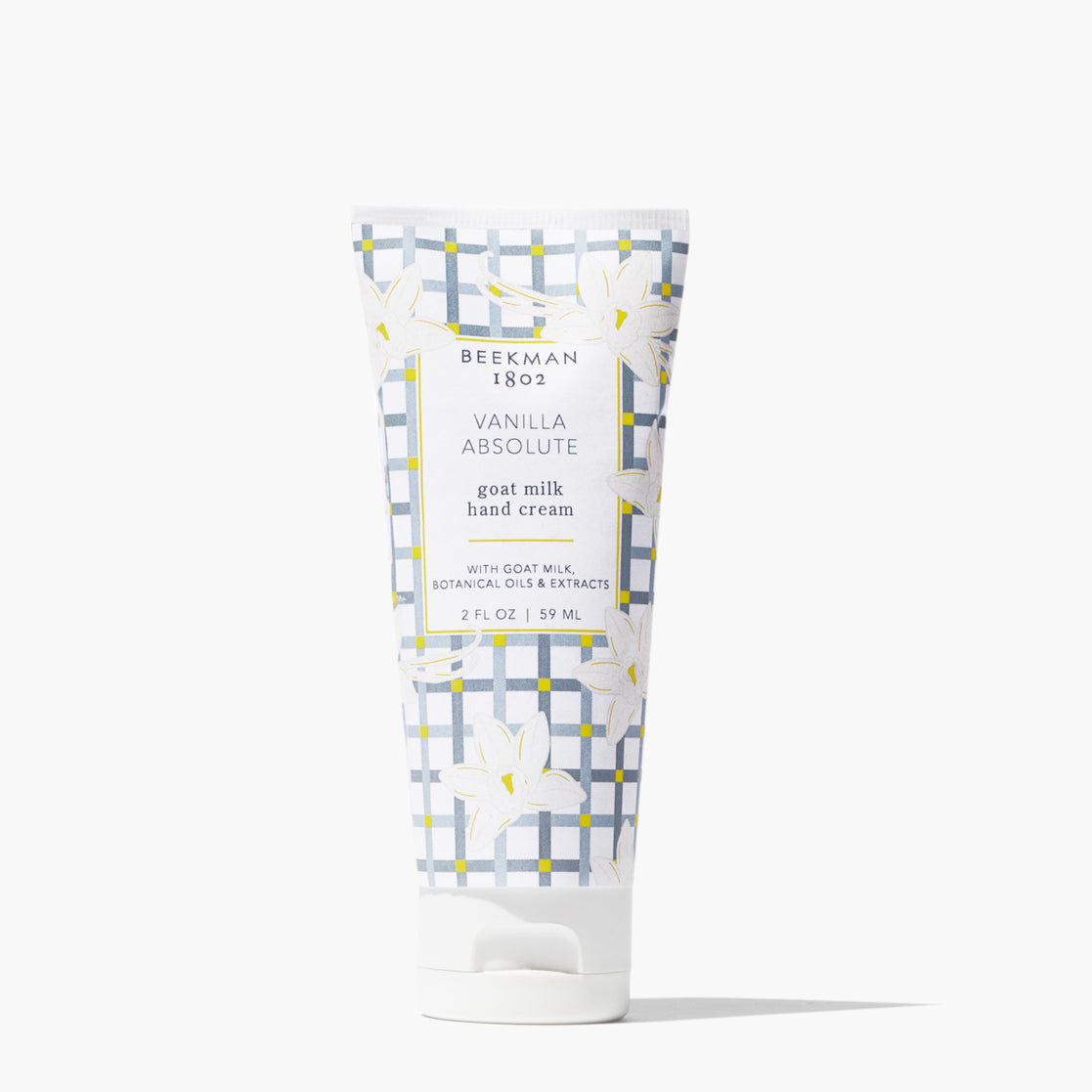 A squeeze tube of Beekman 1802 Vanilla Absolute goat milk hand cream, featuring a white and gray patterned design with yellow accents and white floral illustrations, set against a clean white background. Available at Be Charmed