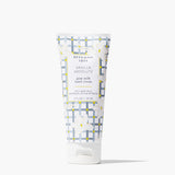A squeeze tube of Beekman 1802 Vanilla Absolute goat milk hand cream, featuring a white and gray patterned design with yellow accents and white floral illustrations, set against a clean white background. Available at Be Charmed