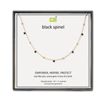 A CAI gold-plated necklace with small black gemstone beads displayed on a white card inside a black gift box. The card shows the brand name 'cai' and the text 'black spinel'. Available at Be Charmed