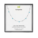 A CAI silver-toned necklace with small turquoise gemstones displayed on a white presentation card inside a black gift box. The card shows the brand name 'cai' and the word 'turquoise', along with the text 'LUCK, LOVE, PROTECTION'. Available at Be Charmed