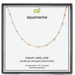 A CAI gold-plated aquamarine gemstone necklace displayed on a white card inside a black gift box. The card features the brand name 'cai' and the word 'aquamarine', along with the message 'FIDELITY, HOPE, LOVE'. Available at Be Charmed