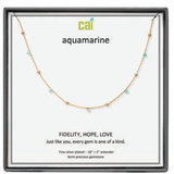 A CAI gold-plated aquamarine gemstone necklace displayed on a white card inside a black gift box. The card features the brand name 'cai' and the word 'aquamarine', along with the message 'FIDELITY, HOPE, LOVE'. Available at Be Charmed