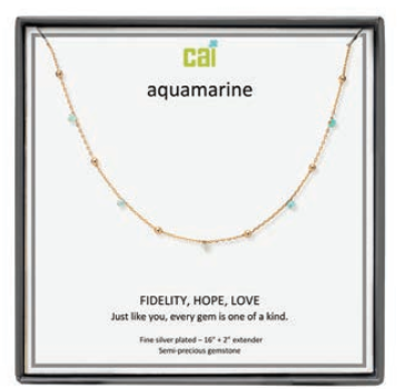 A CAI gold-plated aquamarine gemstone necklace displayed on a white card inside a black gift box. The card features the brand name 'cai' and the word 'aquamarine', along with the message 'FIDELITY, HOPE, LOVE'. Available at Be Charmed