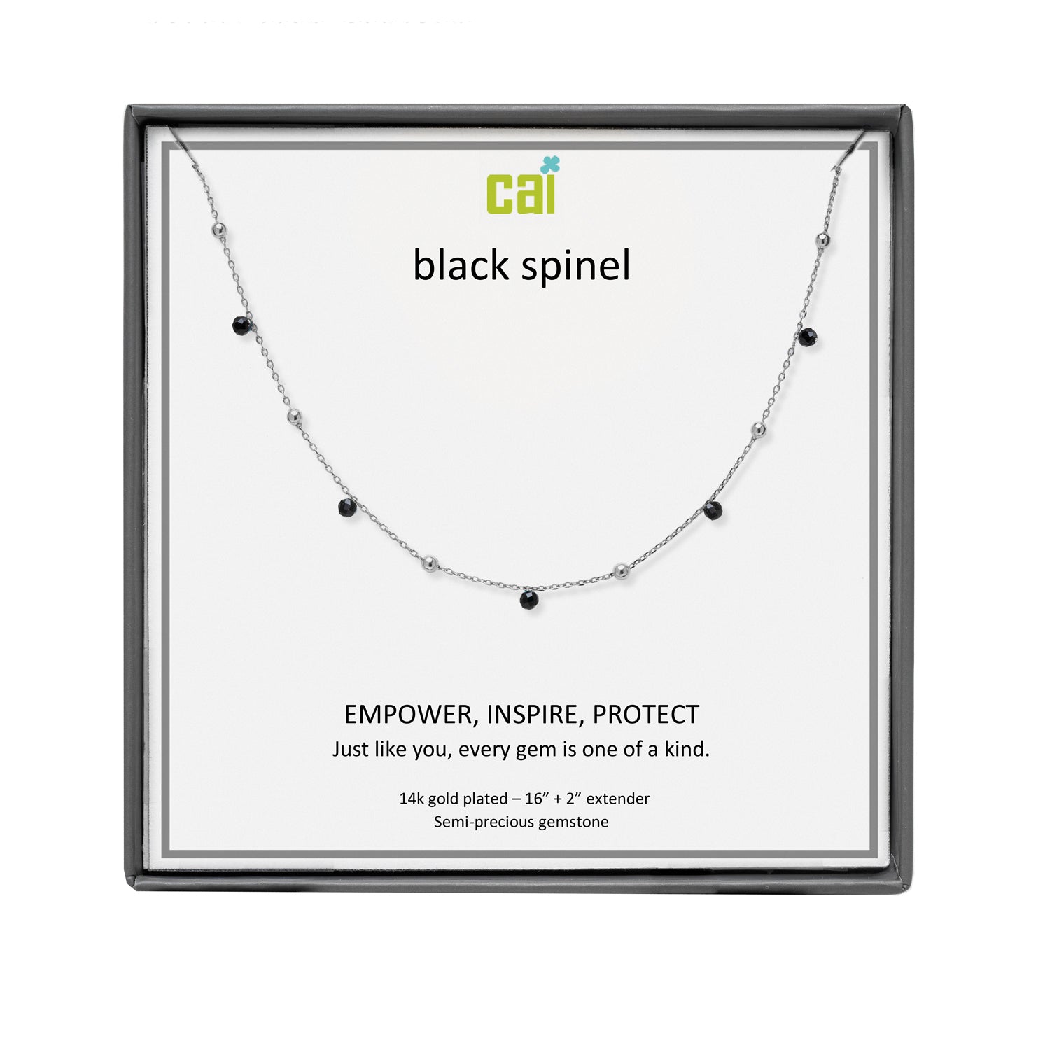 A CAI silver-toned necklace with small black gemstones displayed on a branded white card inside a dark gray square presentation box. The card reads 'cai black spinel' and includes product text below. Available at Be Charmed