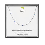 A CAI silver necklace with small blue and clear gemstones displayed on a white card inside a square black gift box. The card is branded with the logo 'cai' and the word 'lapis'. Available at Be Charmed