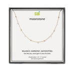 A CAI gold-plated necklace with small clear gemstones displayed on a white card inside a black square gift box. The card shows the brand name 'cai' and the product name 'moonstone'. Available at Be Charmed