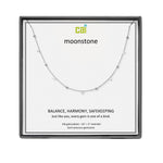 A CAI silver necklace with small spaced beads displayed on a white card inside a square black gift box. The card shows the brand name 'cai' and the product name 'moonstone', along with descriptive text. Available at Be Charmed