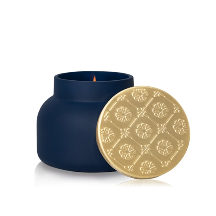 Capri Blue navy blue candle with a gold lid on a white background. Available at Be Charmed