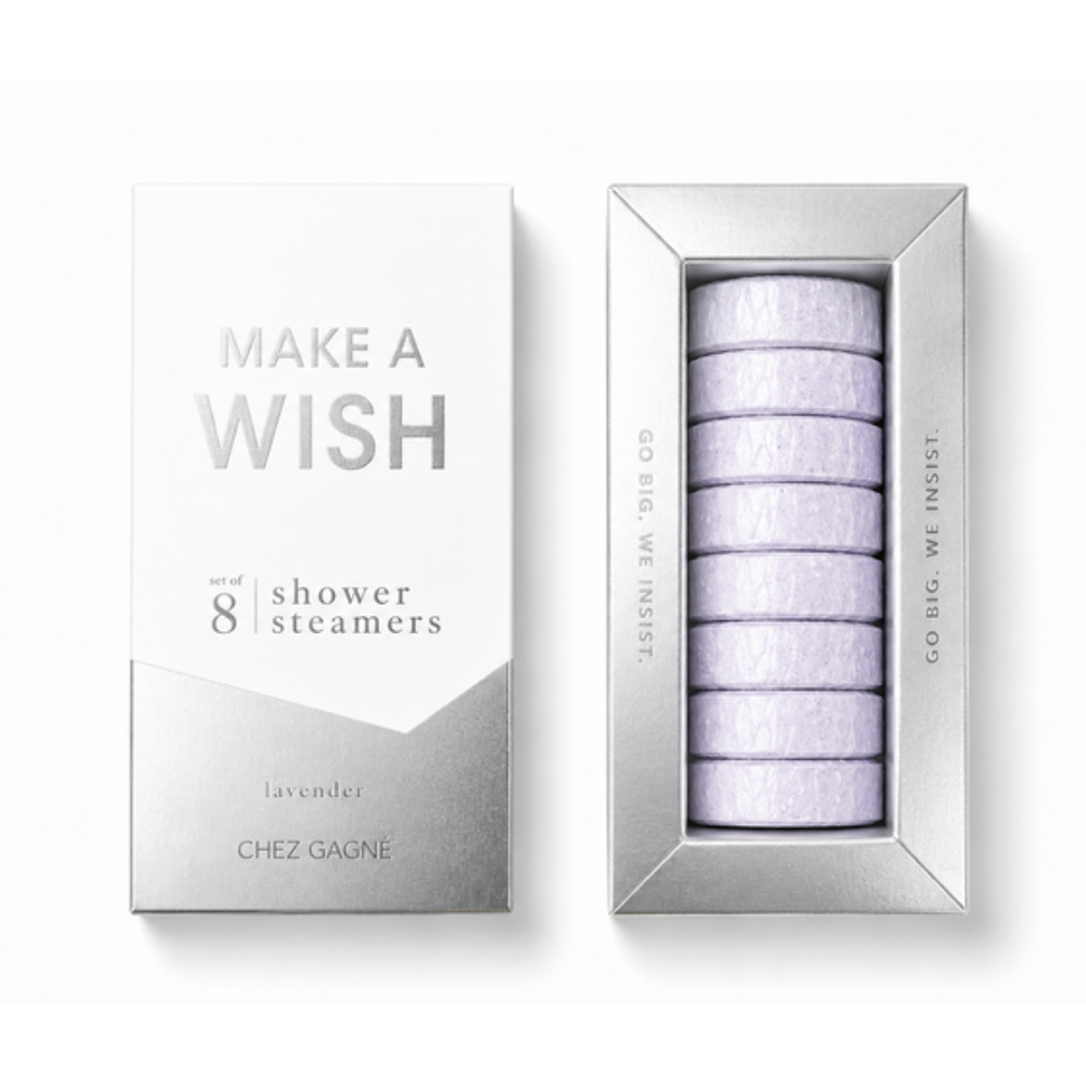 Chez Gagné 'Make A Wish' lavender shower steamers, showing the silver and white outer packaging box alongside the open silver tray containing eight stacked pale lavender circular steamers. Available at Be Chamred