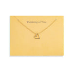 A delicate Demdaco gold necklace with a small open heart pendant, displayed on a yellow card that reads 'Thinking of You.' against a white background. Available at Be Charmed