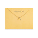 A delicate Demdaco gold necklace with a small open heart pendant, displayed on a yellow card that reads 'Thinking of You.' against a white background. Available at Be Charmed
