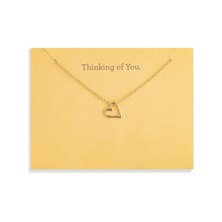 A delicate Demdaco gold necklace with a small open heart pendant, displayed on a yellow card that reads 'Thinking of You.' against a white background. Available at Be Charmed