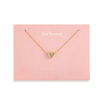 A delicate Demdaco gold necklace with a small heart-shaped pendant, presented on a light pink display card that reads 'Just Because.' against a clean white background. Available at Be Charmed