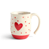 An off-white Demdaco ceramic mug with a curved handle, decorated with a large red heart, red polka dots, and a red base, with the word 'merry' printed inside. Available at Be Charmed