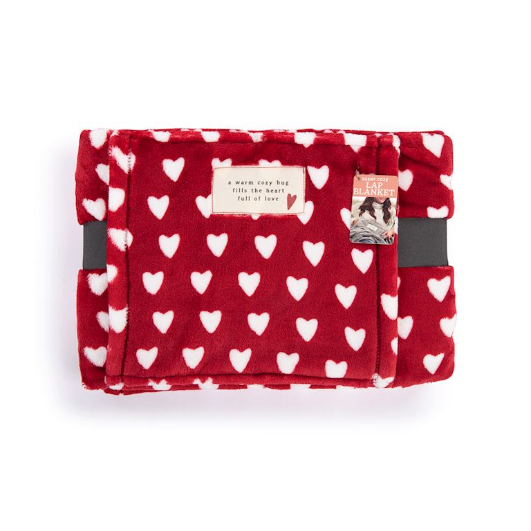 A folded Demdaco red plush blanket with a white heart pattern, featuring a small cream label and a decorative tag on the front, set against a plain white background. Available at Be Charmed