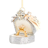 A Demdaco silver glitter ring box ornament with a gold ring displayed inside, adorned with clear rhinestones and a cream hanging ribbon that reads 'Happy Engagement'. Available at Be Charmed