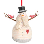 A festive Demdaco snowman Christmas ornament with a cream-colored textured body, black top hat with silver glitter trim, a cream scarf, brown twig arms, two red glitter birds, and a red hanging ribbon. Available at Be Charmed