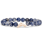 A beaded stretch Fahlo bracelet featuring round blue and white marbled beads with a small, smooth off-white dolphin charm, displayed on a clean white background. Available at Be Charmed