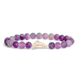 A beaded stretch Fahlo bracelet made of round purple and lavender marbled beads with a small light beige Dolpin charm, shown on a plain white background. Available at Be Charmed