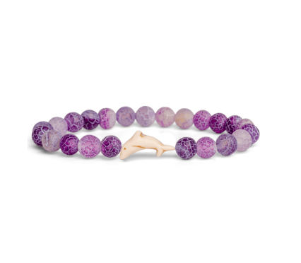 A beaded stretch Fahlo bracelet made of round purple and lavender marbled beads with a small light beige Dolpin charm, shown on a plain white background. Available at Be Charmed