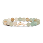 A beaded stretch Fahlo bracelet featuring natural stone beads in muted sage green, cream, and tan, with a small carved white dolphin charm at the center, shown on a plain white background. Available at Be Charmed