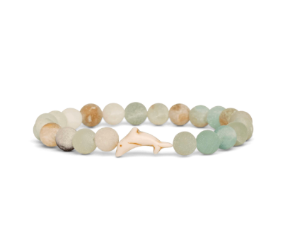 A beaded stretch Fahlo bracelet featuring natural stone beads in muted sage green, cream, and tan, with a small carved white dolphin charm at the center, shown on a plain white background. Available at Be Charmed
