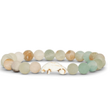 A beaded stretch Fahlo  bracelet featuring natural stone beads in soft sage green, cream, and light brown, with a manatee charm at the center, displayed on a clean white background. Available at Be Charmed