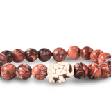 A beaded stretch fahlo bracelet made of round reddish-brown and black marbled beads with a small carved off-white elephant charm in the center, shown on a white background. Available at Be Charmed