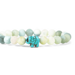 A beaded stretch fahlo bracelet featuring light green, white, and pale blue-green round beads with a small turquoise elephant charm in the center, set against a plain white background. Available at Be Charmed