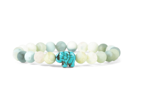 A beaded stretch fahlo bracelet featuring light green, white, and pale blue-green round beads with a small turquoise elephant charm in the center, set against a plain white background. Available at Be Charmed