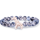 A beaded stretch Fahlo bracelet featuring glossy marbled blue, gray, and white beads with a small white giraffe charm set against a plain white background. Available at Be Charmed