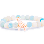 A beaded stretch Fahlo bracelet featuring light blue, white, and pale green marbled round beads, with a small giraffe charm in the center, set against a plain white background. Available at Be Charmed