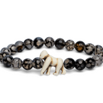 A Fahlo beaded bracelet featuring dark, marbled round beads and a small white carved gorilla charm, displayed on a clean white background. Available at Be Charmed