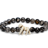 A Fahlo beaded bracelet featuring dark, marbled round beads and a small white carved gorilla charm, displayed on a clean white background. Available at Be Charmed