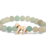 A beaded stretch Fahlo bracelet featuring matte sage green and cream stone beads, with a small carved ivory gorilla figure at the front center, set against a plain white background. Available at Be Charmed