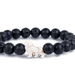 A beaded stretch Fahlo bracelet made of black porous lava stones with a small white lion charm in the center, shown on a plain white background. Available at Be Charmed