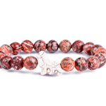 A beaded stretch Fahlo bracelet featuring round reddish-brown and black marbled beads with a small white ceramic lion charm in the center, displayed on a clean white background. Available at Be Charmed