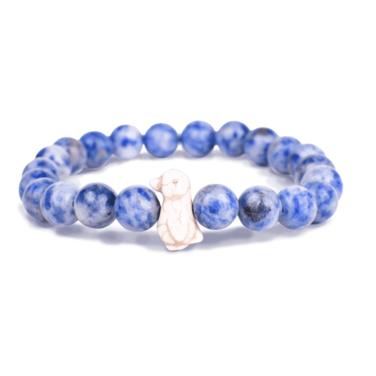 A beaded stretch Fahlo bracelet made of round blue and white marbled gemstone beads, featuring a small white carved penguin charm in the center, set against a plain white background. Available at Be Charmed