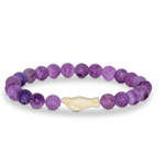 A beaded stretch Fahlo bracelet featuring round purple marbled beads and a central cream-colored bone-shaped seal bead, displayed on a clean white background. Available at Be Charmed