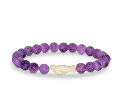 A beaded stretch Fahlo bracelet featuring round purple marbled beads and a central cream-colored bone-shaped seal bead, displayed on a clean white background. Available at Be Charmed