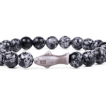 A beaded stretch Fahlo bracelet featuring round black and white speckled beads with a central shark charm, displayed on a clean white background. Available at Be Charmed