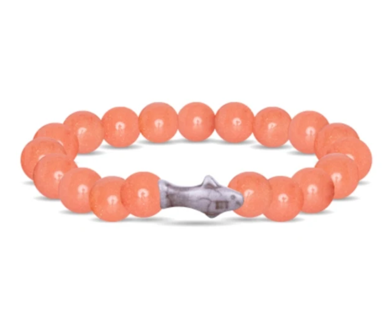 A beaded stretch Fahlo bracelet made of smooth, peachy-orange round beads with a small gray stone shark charm in the center, shown on a plain white background. Available at Be Charmed