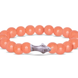 A beaded stretch Fahlo bracelet made of smooth, peachy-orange round beads with a small gray stone shark charm in the center, shown on a plain white background. Available at Be Charmed