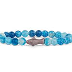 A beaded stretch Fahlo bracelet featuring textured blue and light blue marbled beads, with a central gray shark charm, displayed on a clean white background. Available at Be Charmed