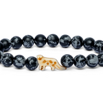 A beaded stretch Fahlo bracelet featuring dark gray and black marbled round beads with a small cream-colored snow leopard charm decorated with brown spots, set against a plain white background. Available at Be Charmed